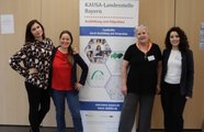 Vier Mitarbeiterinnen der KAUSA-Landesstelle stehen rechts und links neben einem Roll-up zum Projekt.