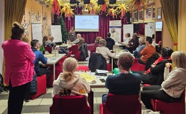 Mehrere Gäste sitzen an ihren Tischen und schauen zum Moderator des Workshops nach vorne.