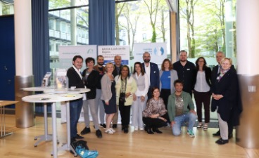 Eine Gruppe der Veranstalter steht nebeneinander im Foyer vor einem KAUSA Plakat