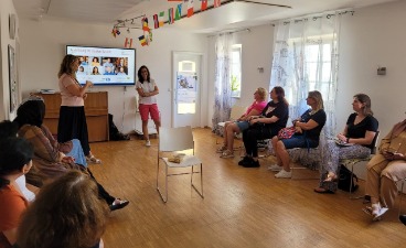 Eine Gruppe von Frauen sitzt an kreisförmig angeordneten Stühlen. Sie blicken nach vorne zur Rednerin vor einer Präsentation.