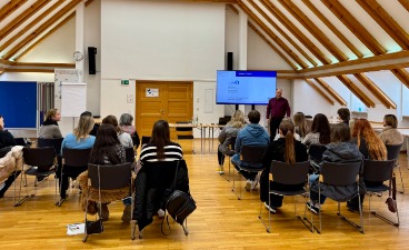 Mehrere Gäste sind von hinten zu sehen und schauen nach vorne zum Redner, der vor einer Präsentation steht.